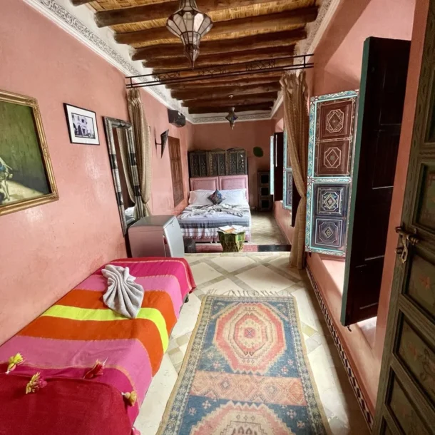 Spacious-riad-bedroom-with-pink-tadelakt-walls_-wooden-ceiling-beams_-colorful-textiles_-Berber-rugs