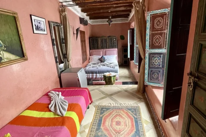 Spacious-riad-bedroom-with-pink-tadelakt-walls_-wooden-ceiling-beams_-colorful-textiles_-Berber-rugs