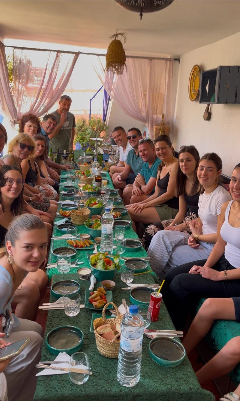Guests-seated-around-a-long-table-sharing-a-Moroccan-meal-on-a-bright-riad-terrace-with-local-décor